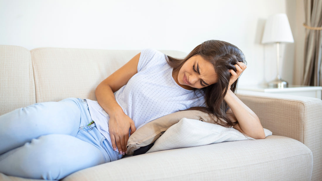 A woman lying on a bed, her hands resting on her abdomen in discomfort, indicating possible abdominal pain or discomfort.