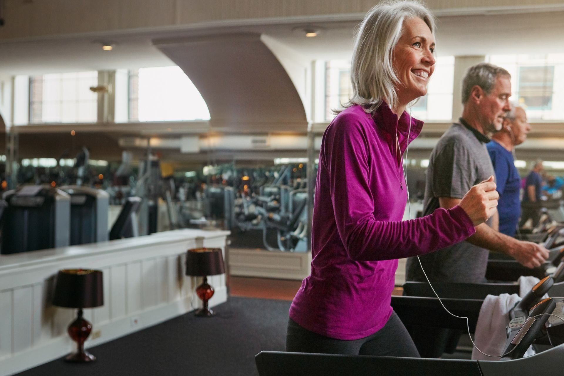 Smiling woman walking on a treadmill in a gym, symbolising active and pain-free living through joint pain therapy for arthritis relief