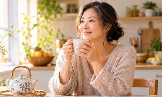 Middle-aged Chinese woman enjoying a warm drink in a peaceful sunlit kitchen.