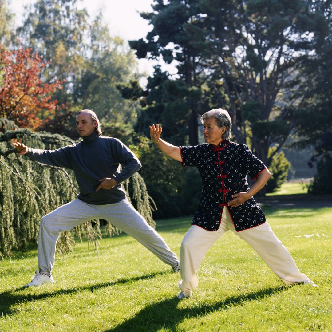 Man and woman practicing tai chi in a park to promote back pain relief and a healthy lifestyle